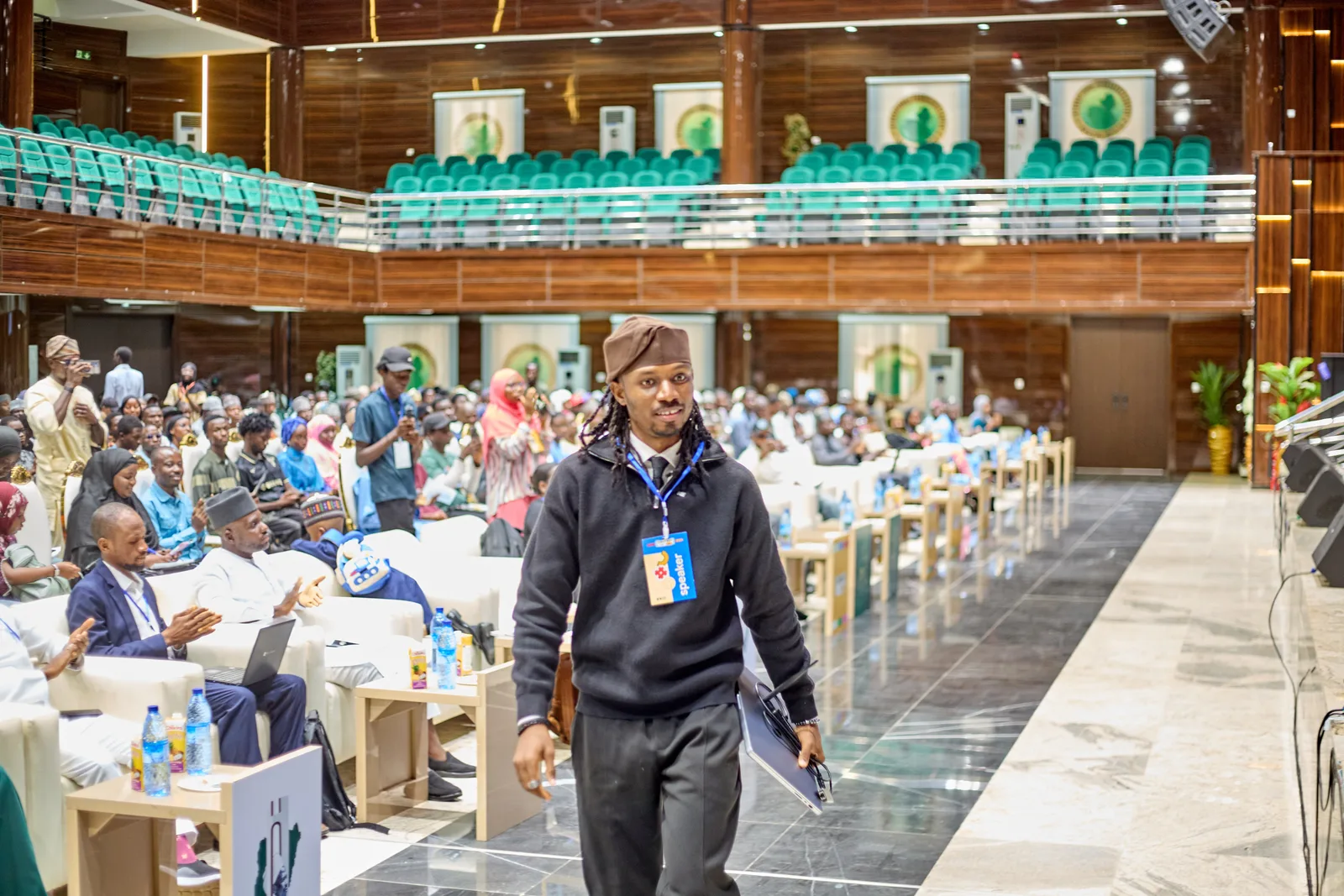 Godson walking down the aisle of the DevFest Bauchi hall with a speaker badge, as the audience applauds